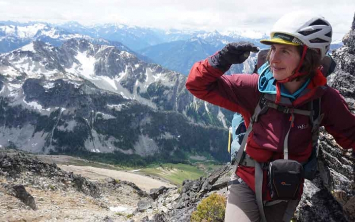 a woman wearing mountaineering gear shades her face with her hand. Snowy mountains are in the background.